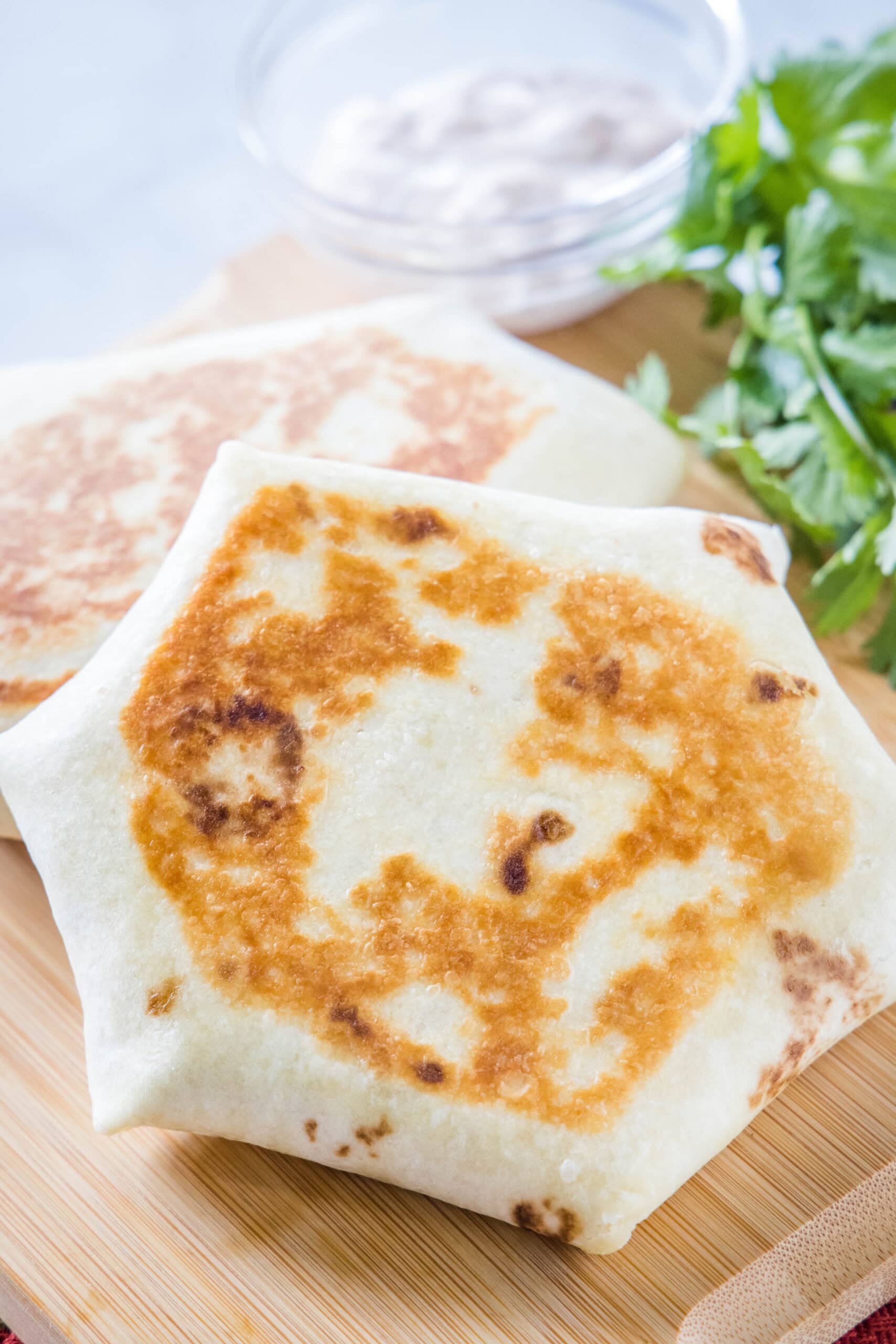 A breakfast crunchwrap propped up against a second crunchwrap on a wooden cutting board.