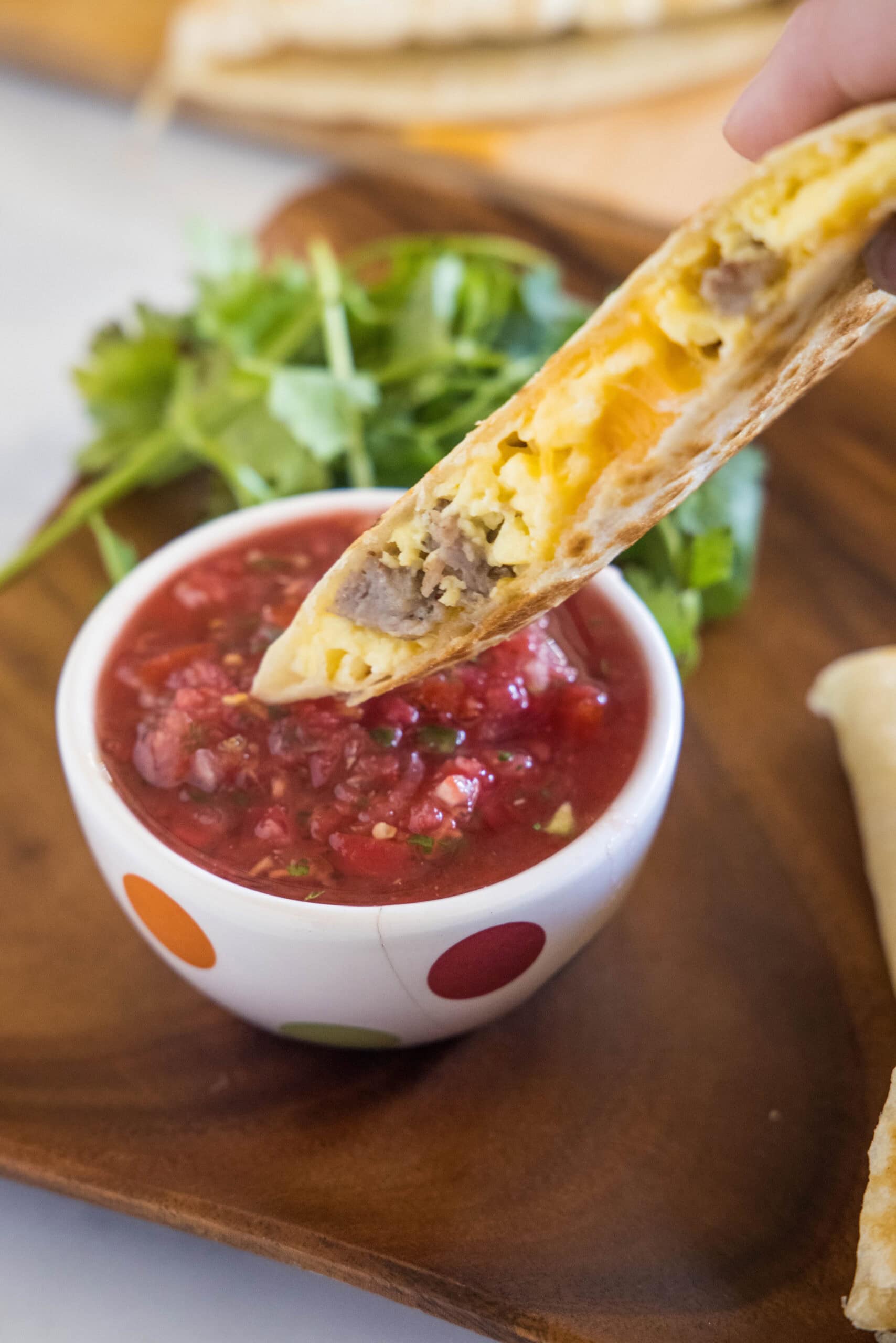A breakfast quesadilla dipped into a bowl of salsa.