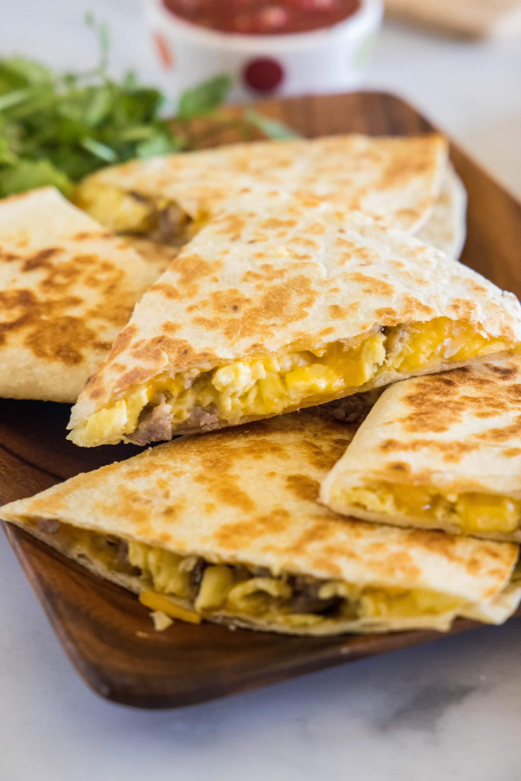 Rise and shine with this easy breakfast quesadilla recipe! Made with eggs, savory sausage, and melty cheese folded between warm tortillas. Breakfast quesadillas stacked on a wooden serving platter.