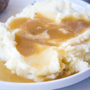 close up of brown gravy over mashed potatoes on a white plate