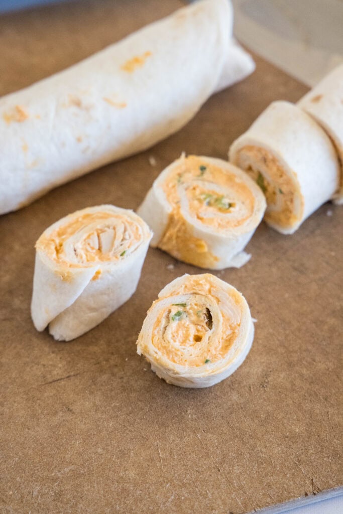 Sliced Buffalo chicken pinwheels next to a rolled up tortilla.