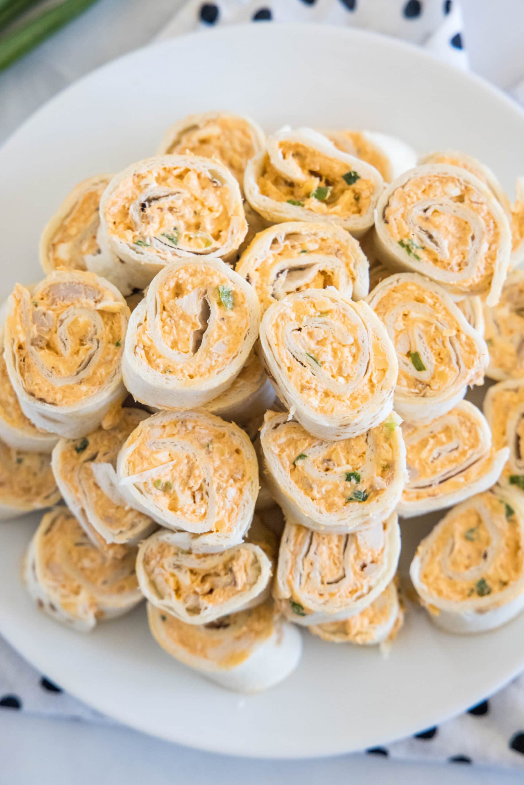 Overhead view of Buffalo chicken pinwheels stacked on a white plate.