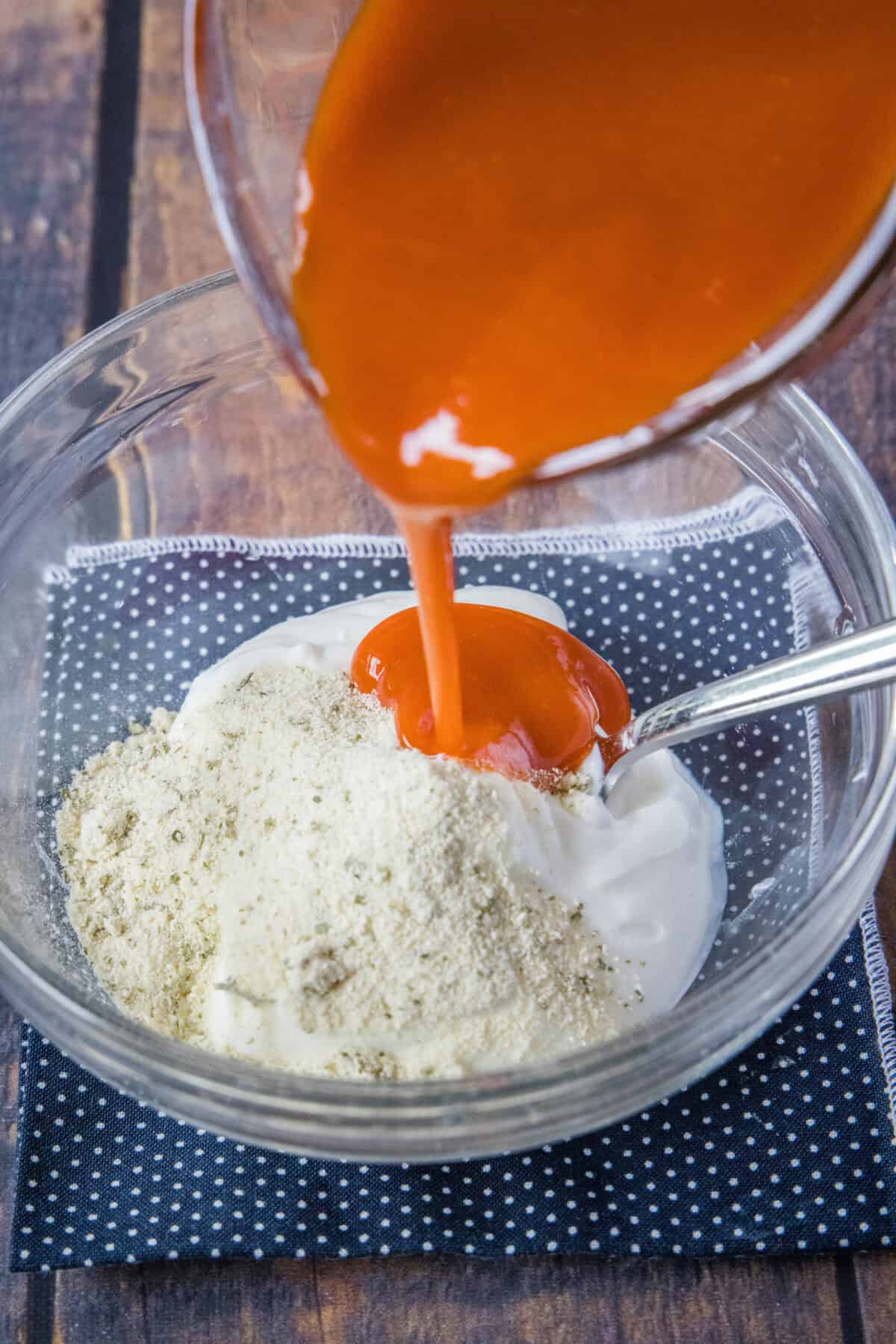 buffalo sauce being poured into bowl with mayo and ranch seasoning