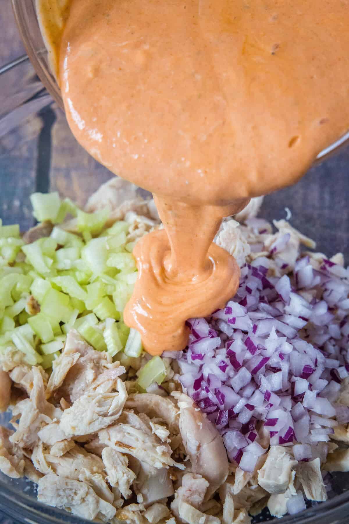 pouring buffalo dressing over chicken, onions and celery