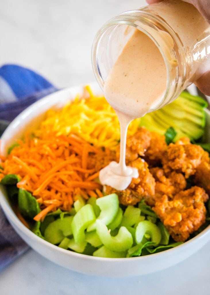 pouring spicy ranch over buffalo chicken salad