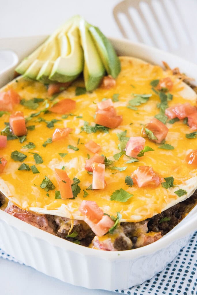 burrito casserole topped with tomatoes, cilantro and avocado
