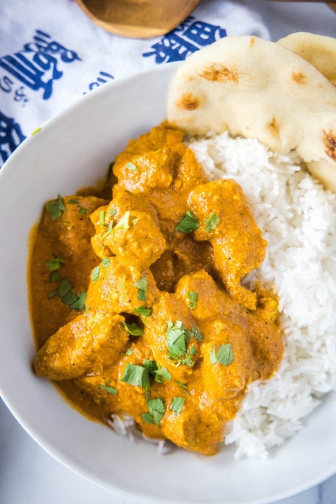 looking down on a bowl of butter chicken curry, rice and naan bread