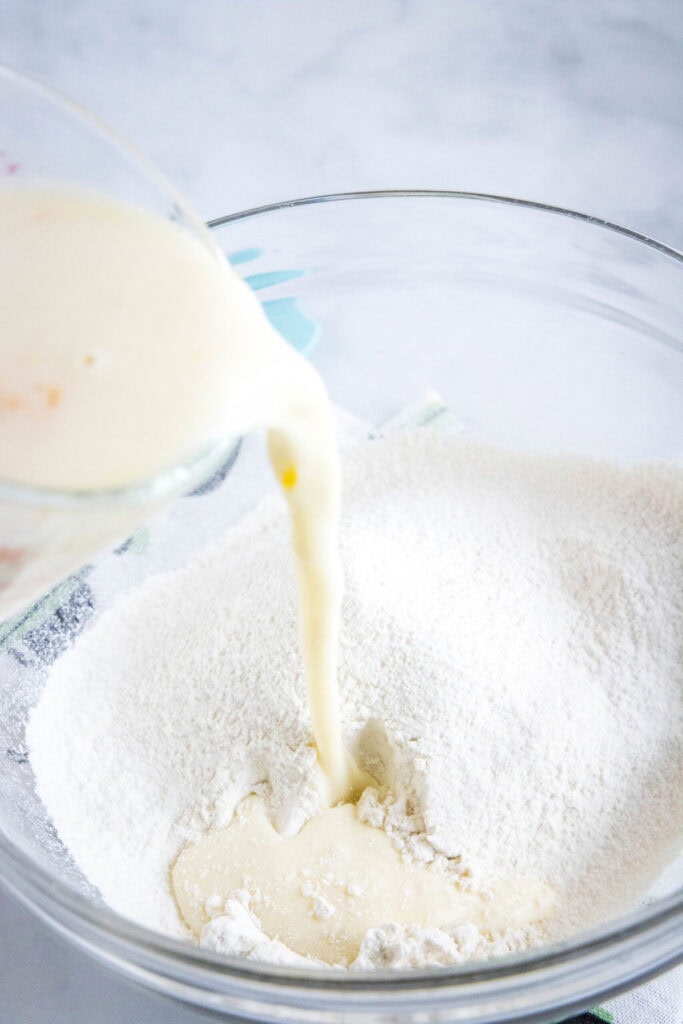 A pyrex pouring a liquid mixture into a flour mixture