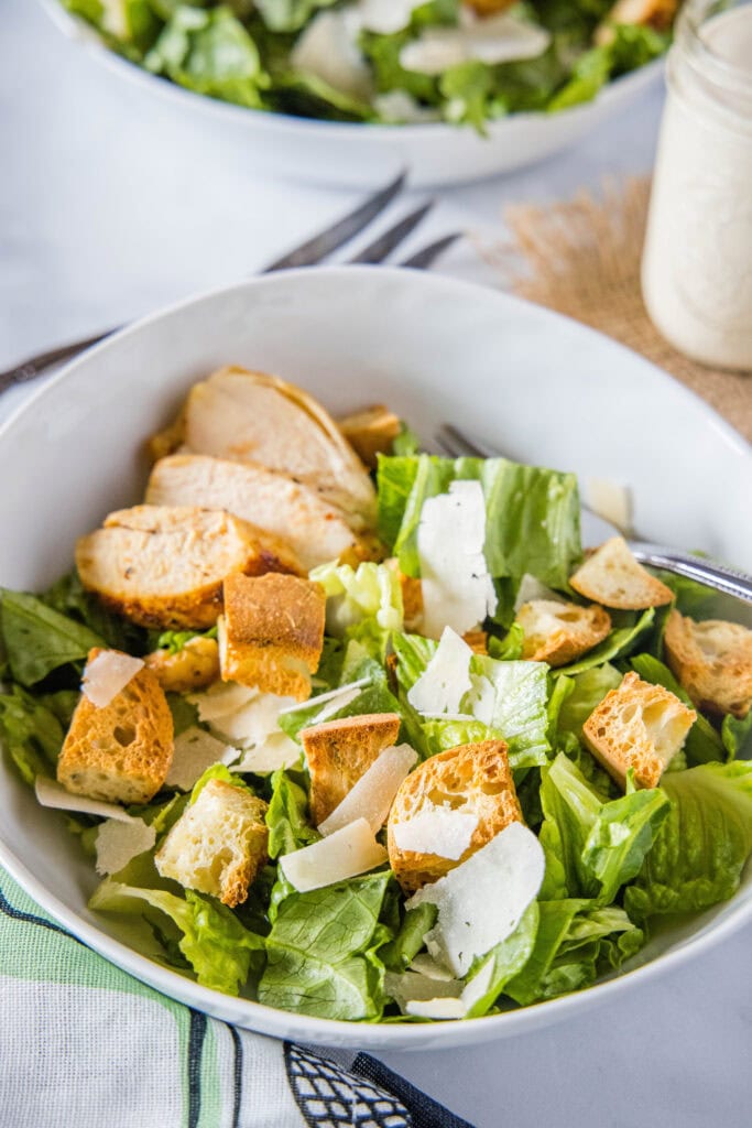 a small bowl with salad in it, caesar salad in mason jar in background