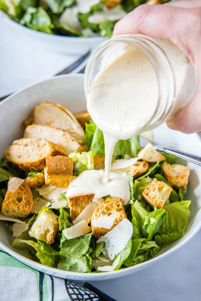 pouring caesar dressing on salad