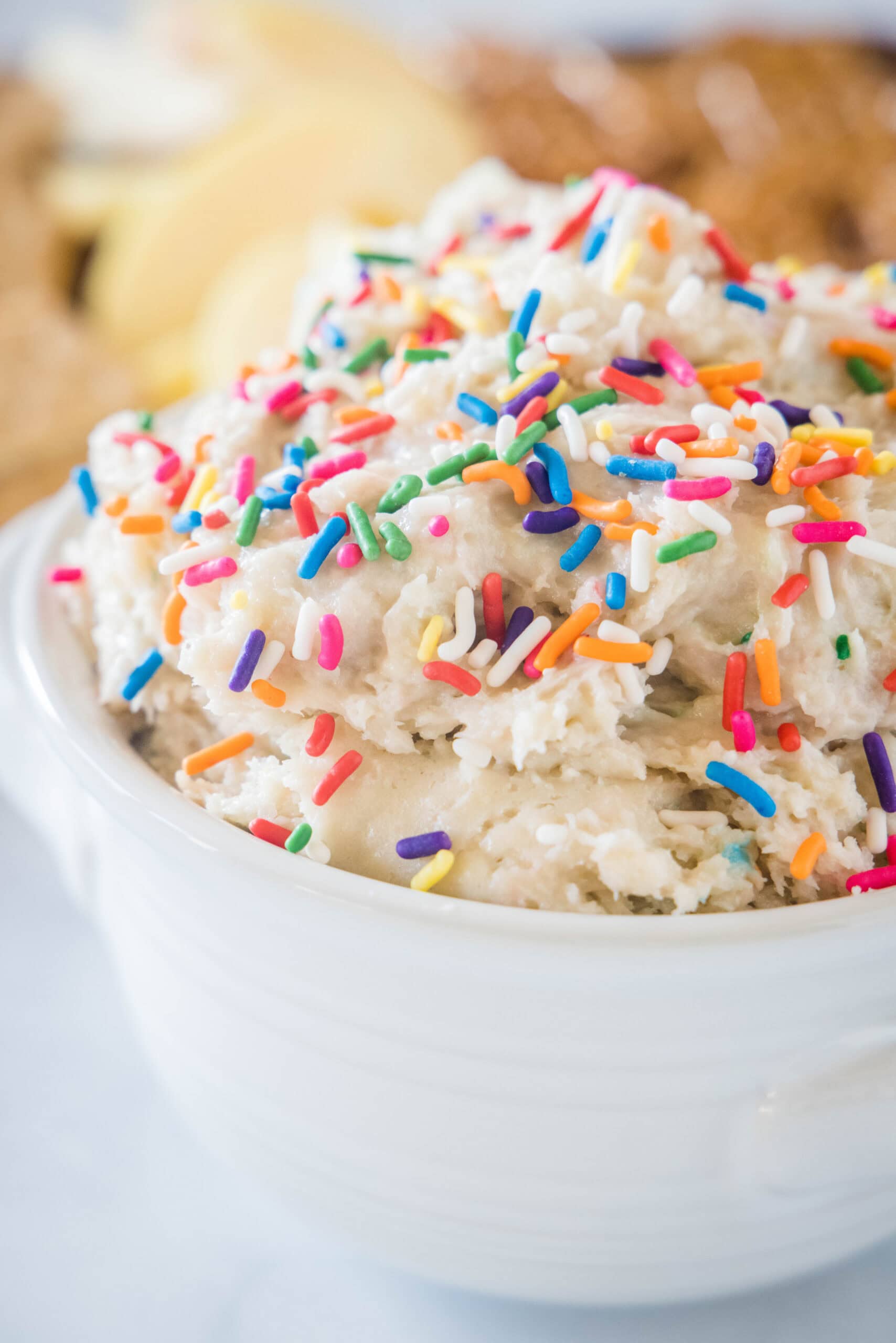 Cake batter dip in a white bowl topped with sprinkles, with a platter of cookies in the background.
