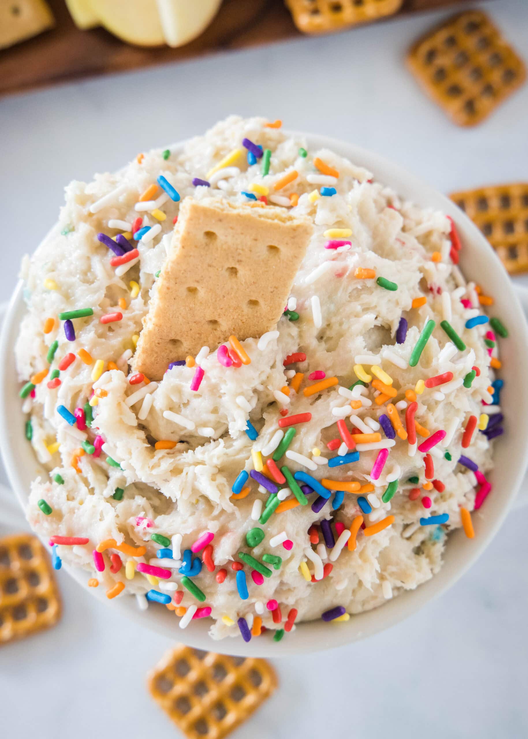 Overhead view of cake batter dip in a white bowl with a cookie stuck into the top.