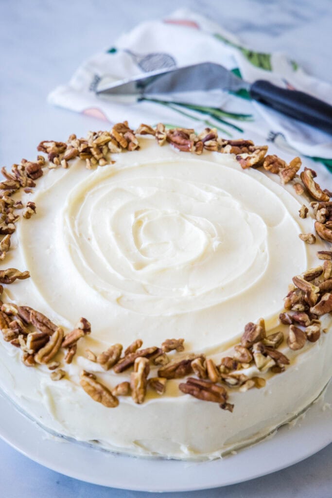 A whole carrot cake frosted with cream cheese frosting and garnished with chopped pecans.