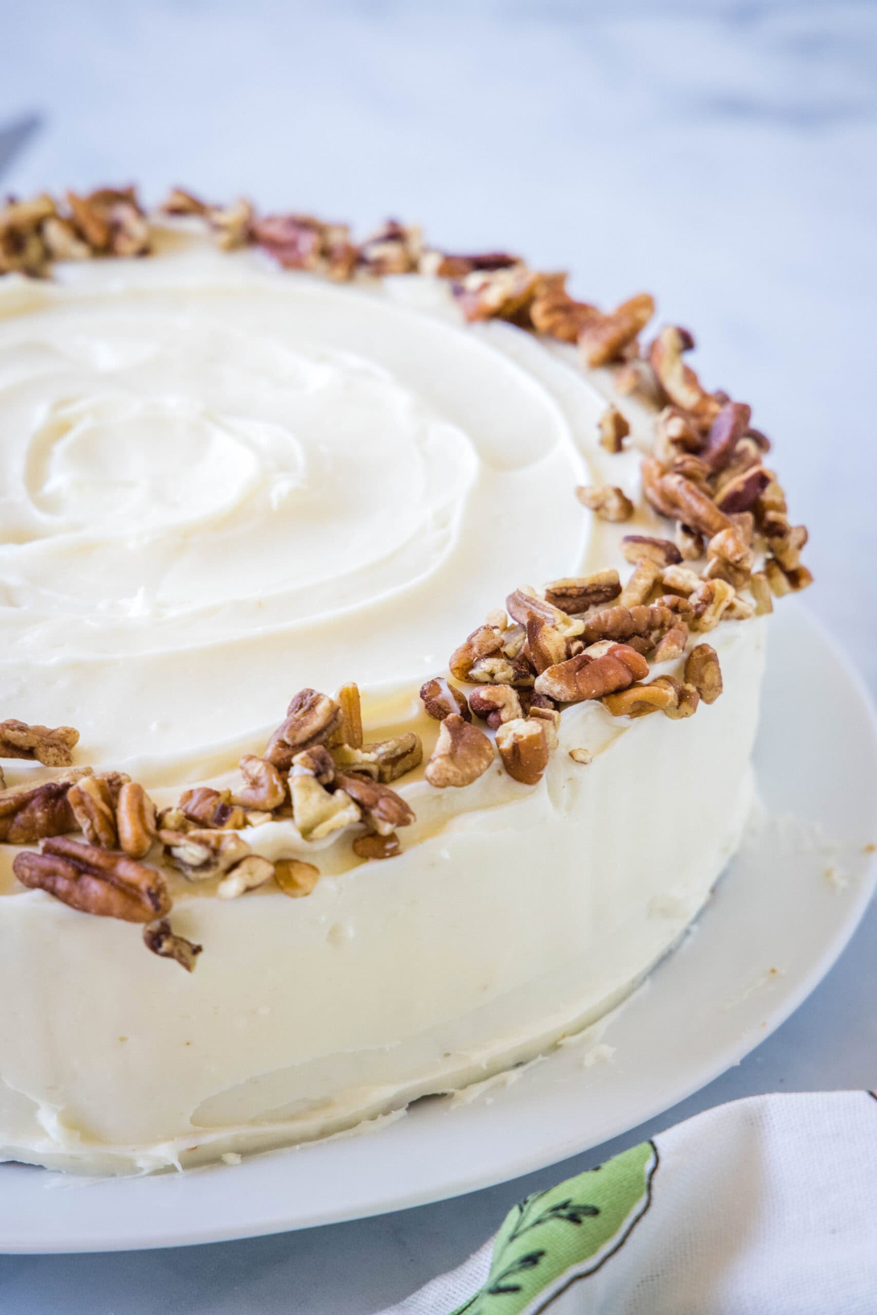 A whole carrot cake frosted with cream cheese frosting and garnished with chopped pecans.