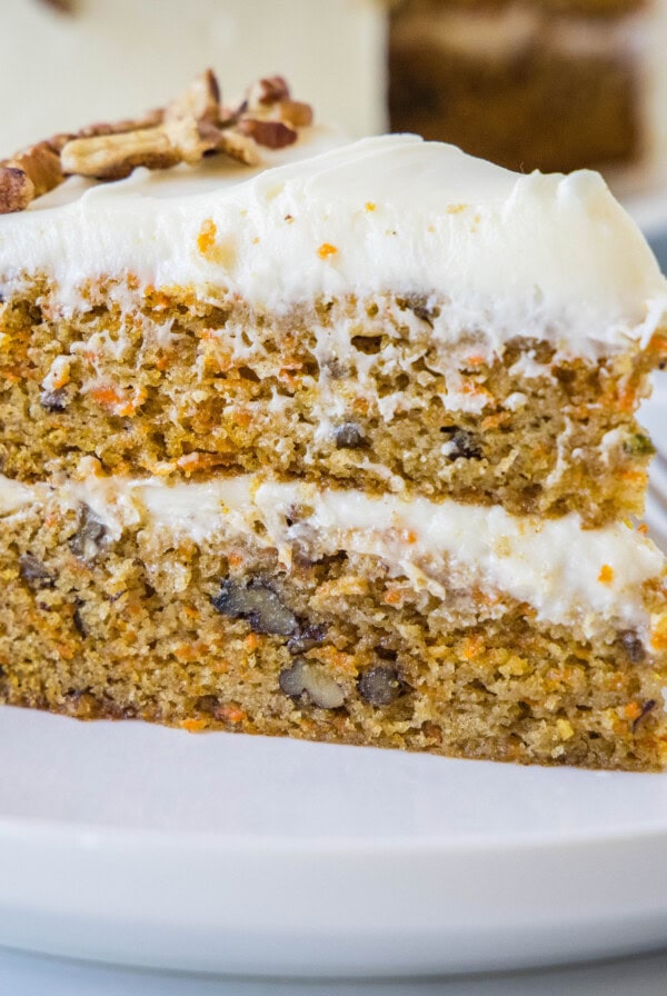 A slice of frosted carrot cake on a white plate next to a fork.