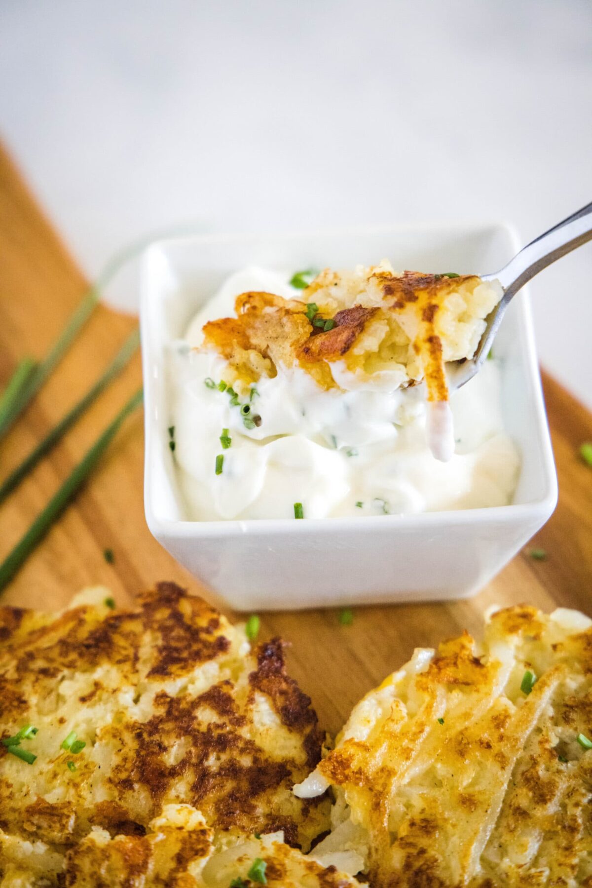 A fork dipping a piece of cauliflower fritter into a bowl of sauce, on a cutting board with more fritters