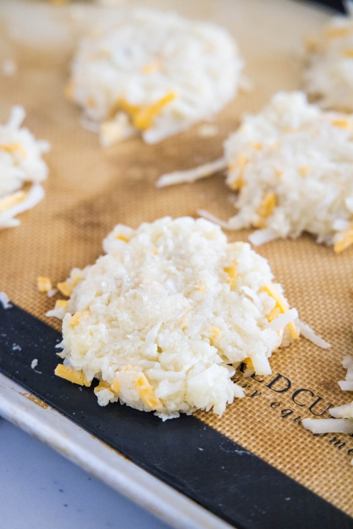 Portioned cauliflower fritters, uncooked, on a baking sheet