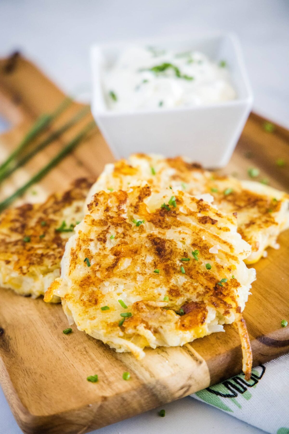 Close up of cauliflower fritters on a cutting board with a bowl of sauce behind them