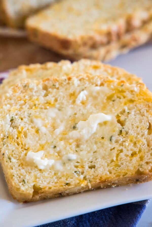 Close up of a slice of cheesy quick bread spread with butter, with more slices in the background.