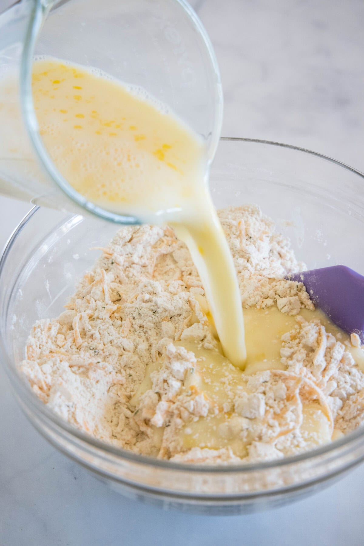 Wet ingredients being poured into a bowl of dry cheesy bread ingredients.