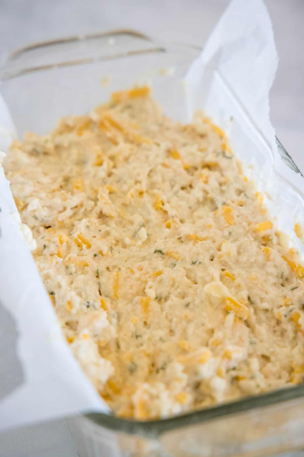 Cheesy bread batter added to a parchment-lined glass loaf pan.