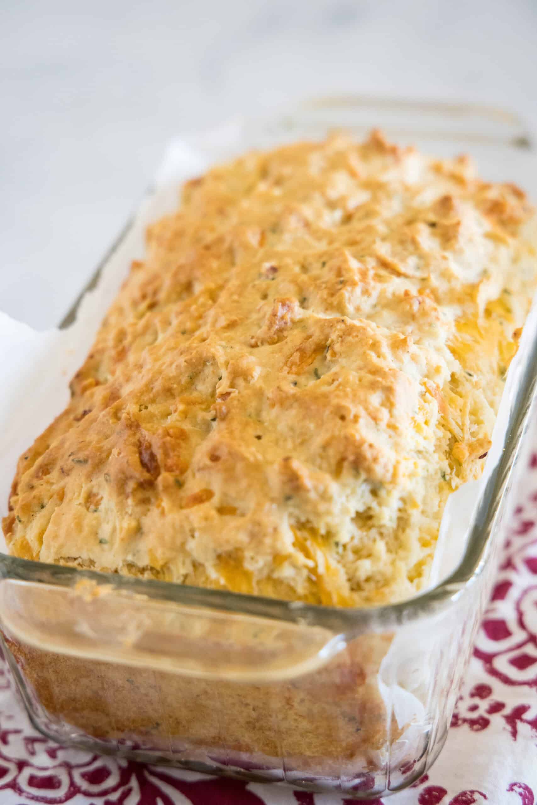 Baked cheesy quick bread inside a parchment-lined glass loaf pan.