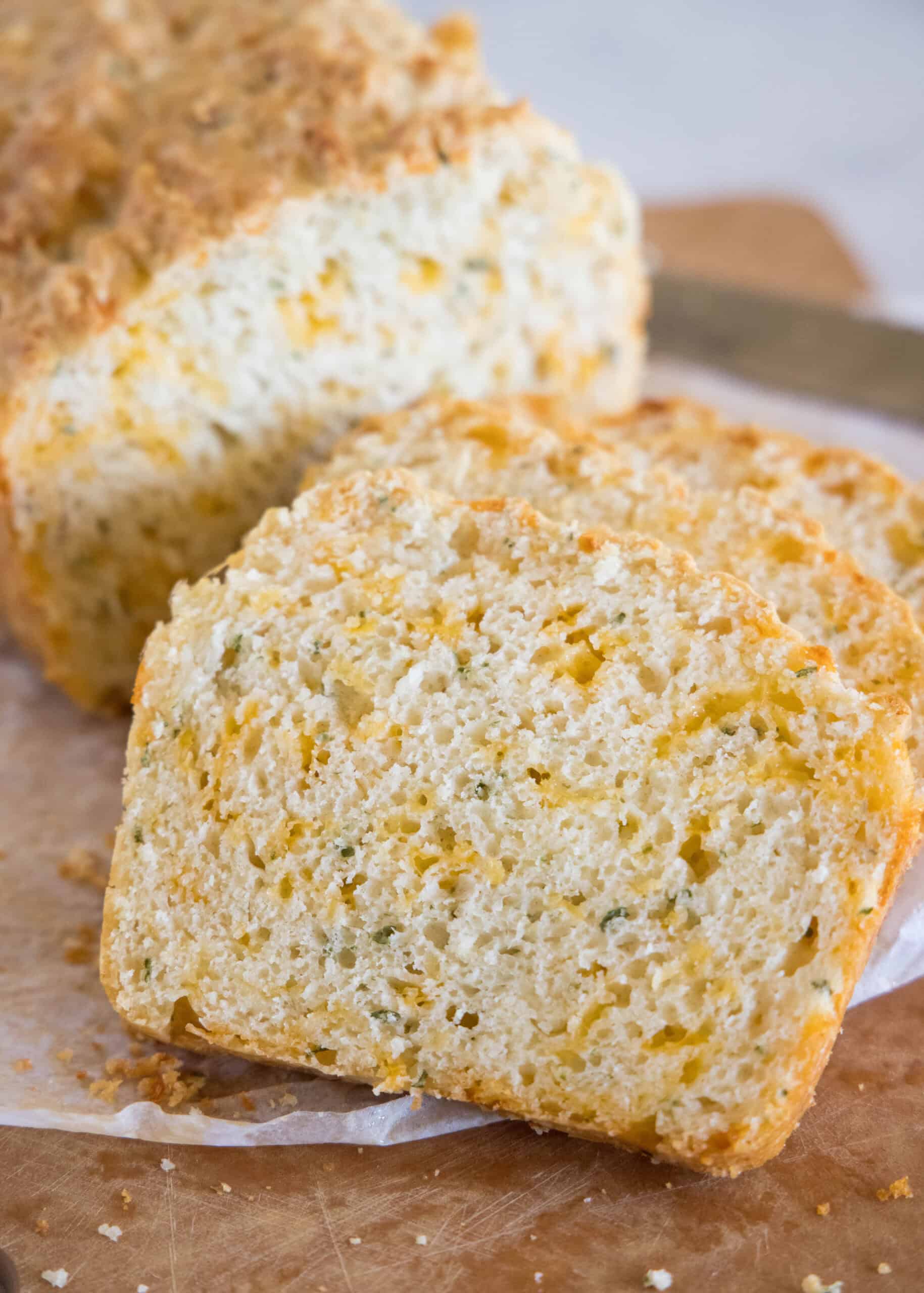 Slices of cheddar quick bread cut from the end of a loaf on a parchment-lined wooden cutting board.