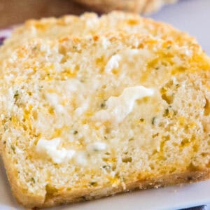 Close up of a slice of cheesy quick bread spread with butter.