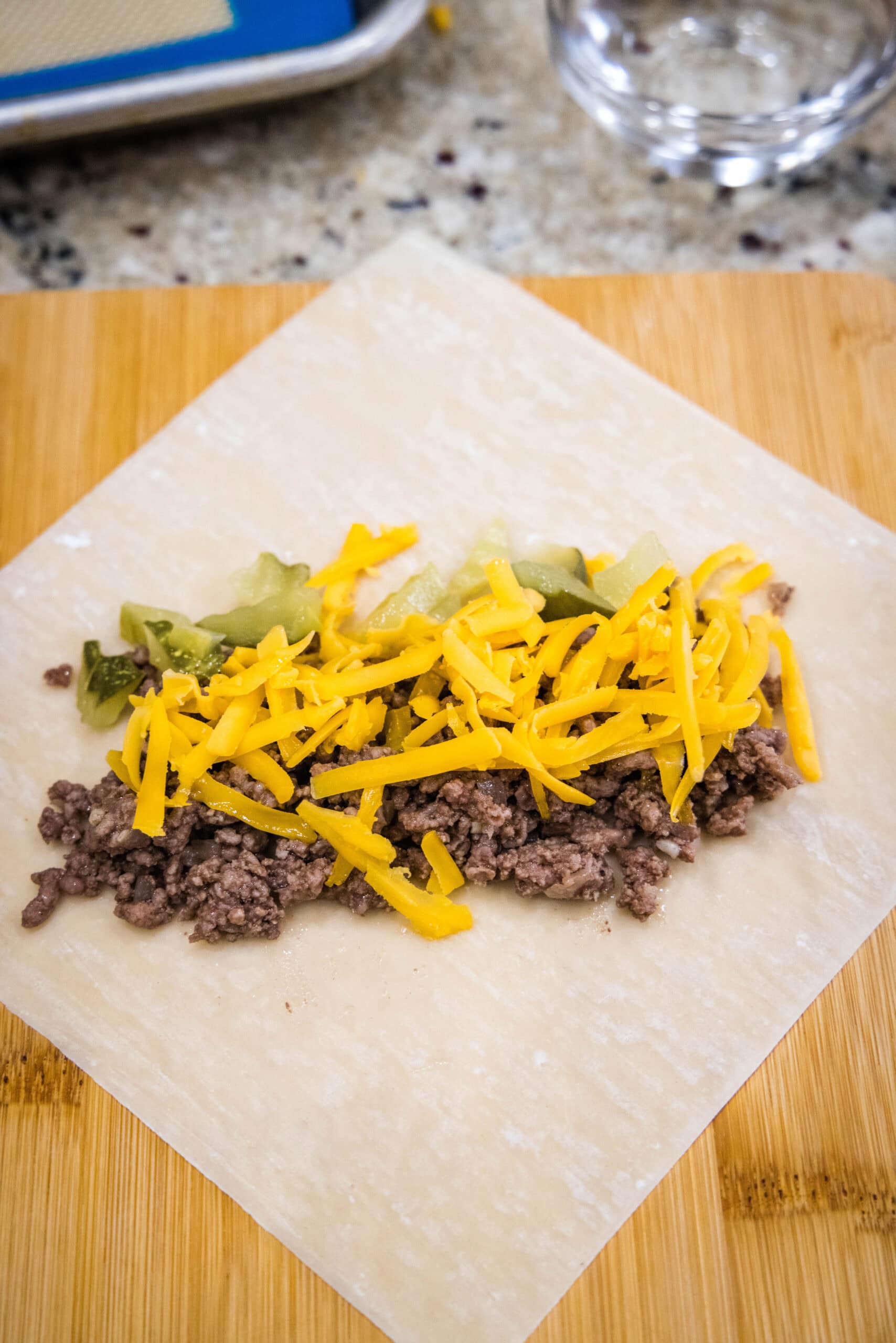 Cheeseburger filling topped with shredded cheese on top of an egg roll wrapper.