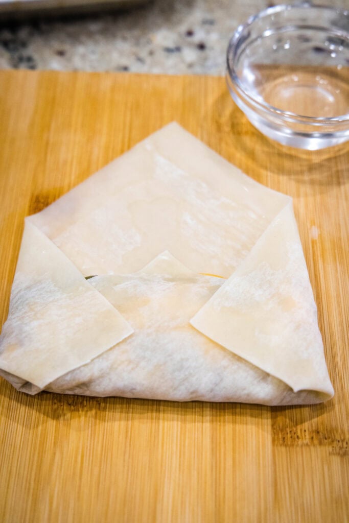 A partially folded cheeseburger egg roll on a wooden surface.