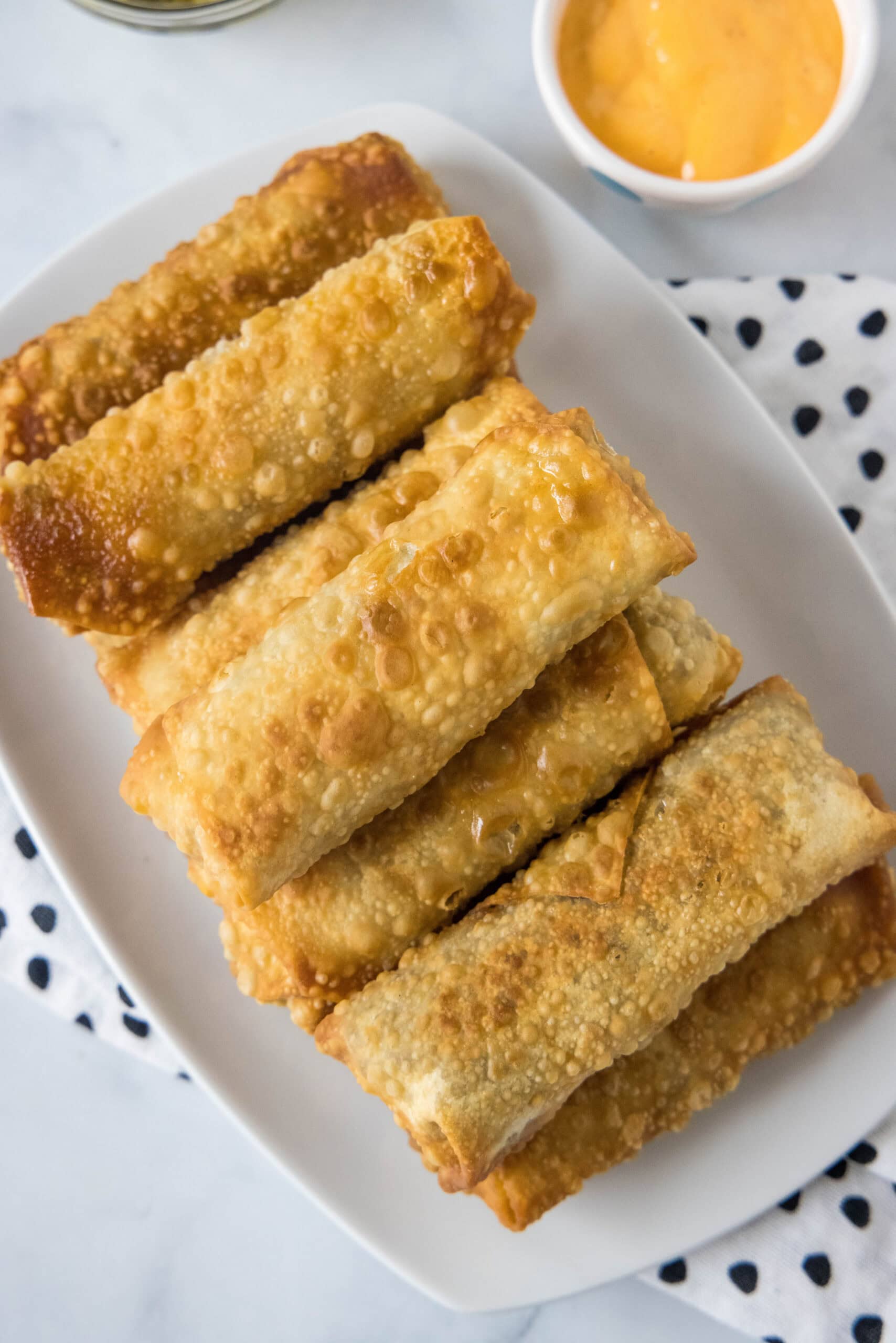 Overhead view of cheeseburger egg rolls on a platter next to a bowl of dipping sauce.