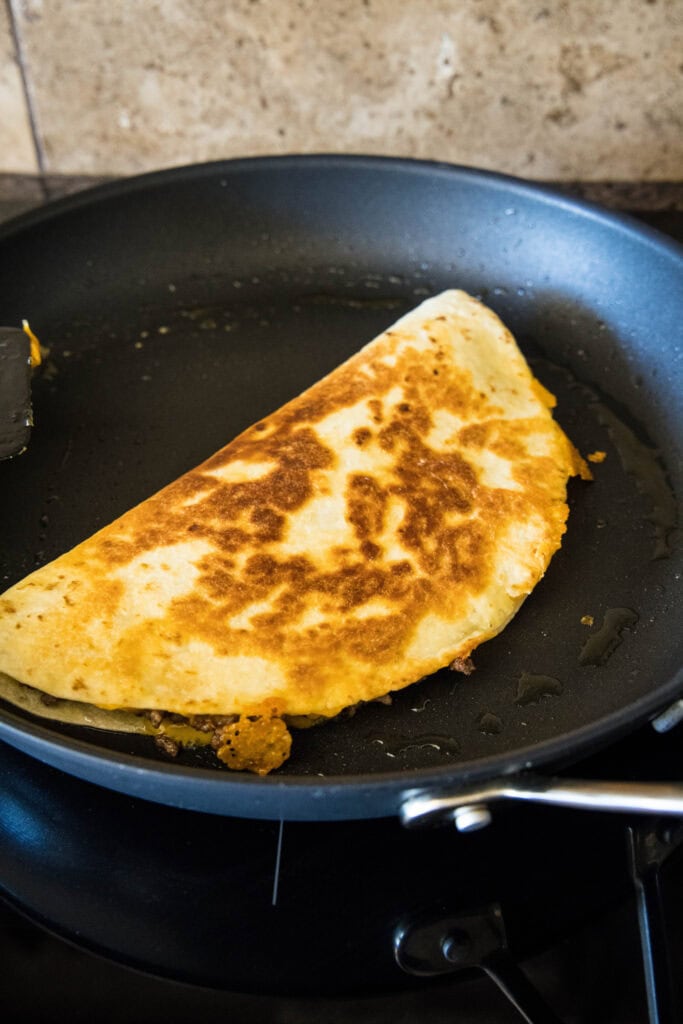 A cheeseburger quesadilla frying in a black skillet.