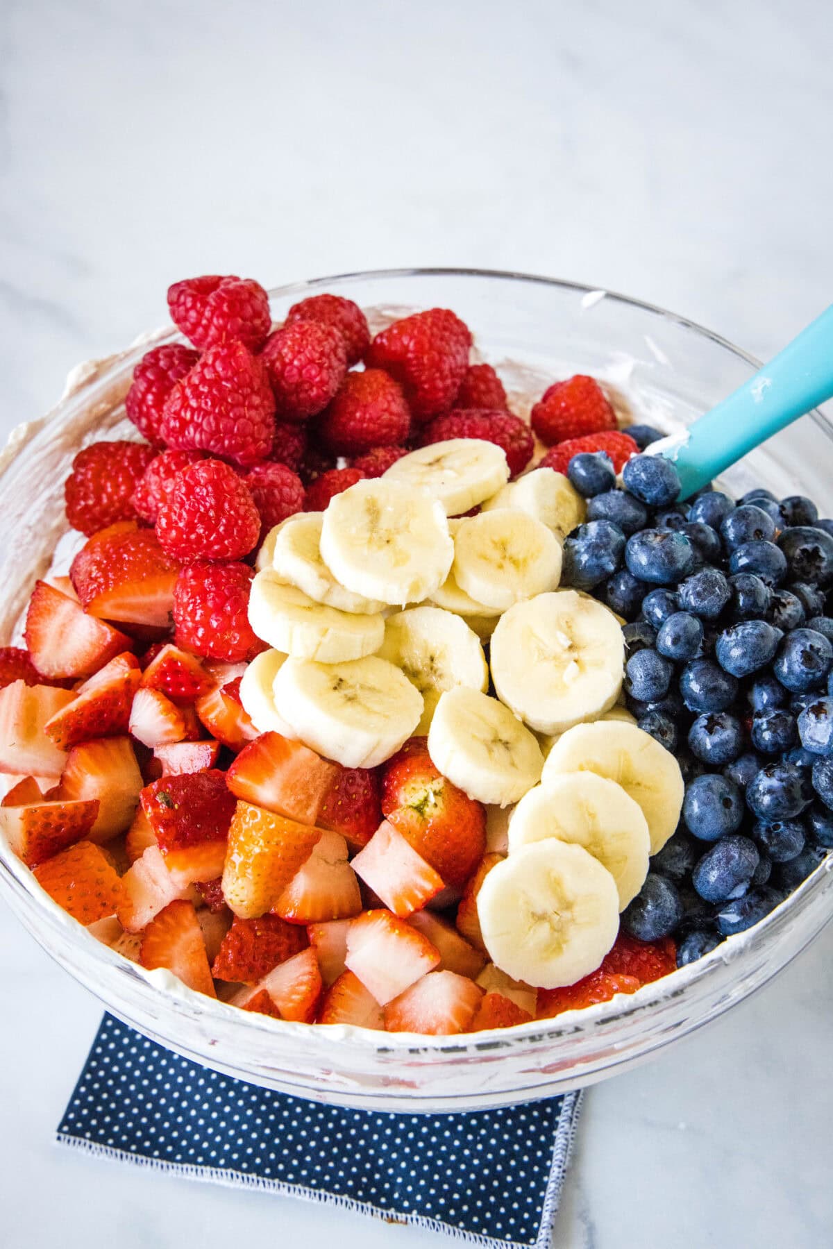 Fresh berries and bananas added to a bowl of whipped cream cheese dressing.
