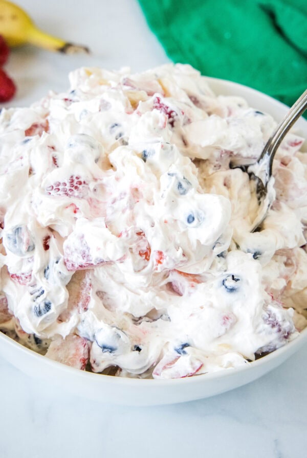 Cheesecake fruit salad in a bowl with a spoon for serving.