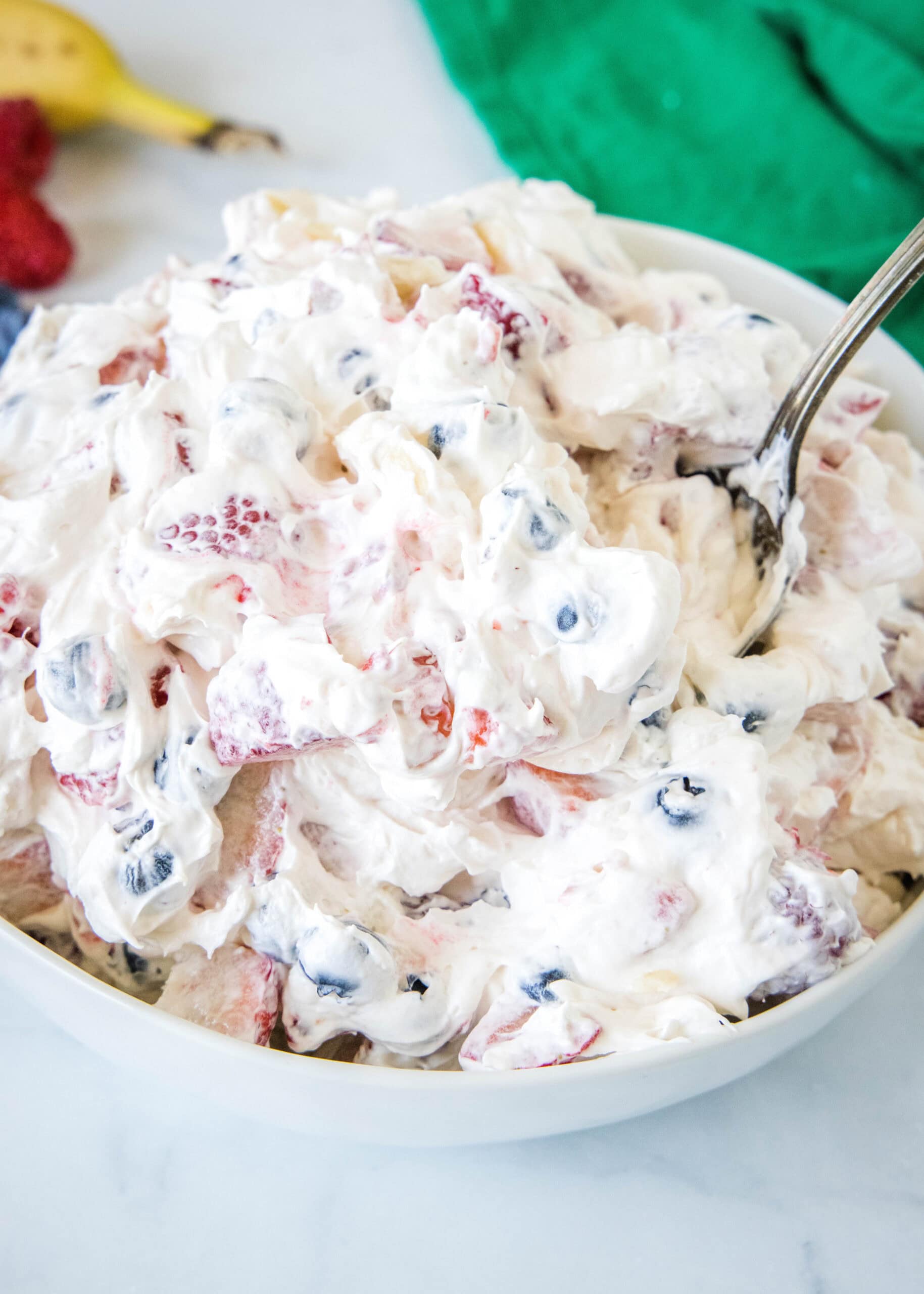 Cheesecake fruit salad in a bowl with a spoon for serving.
