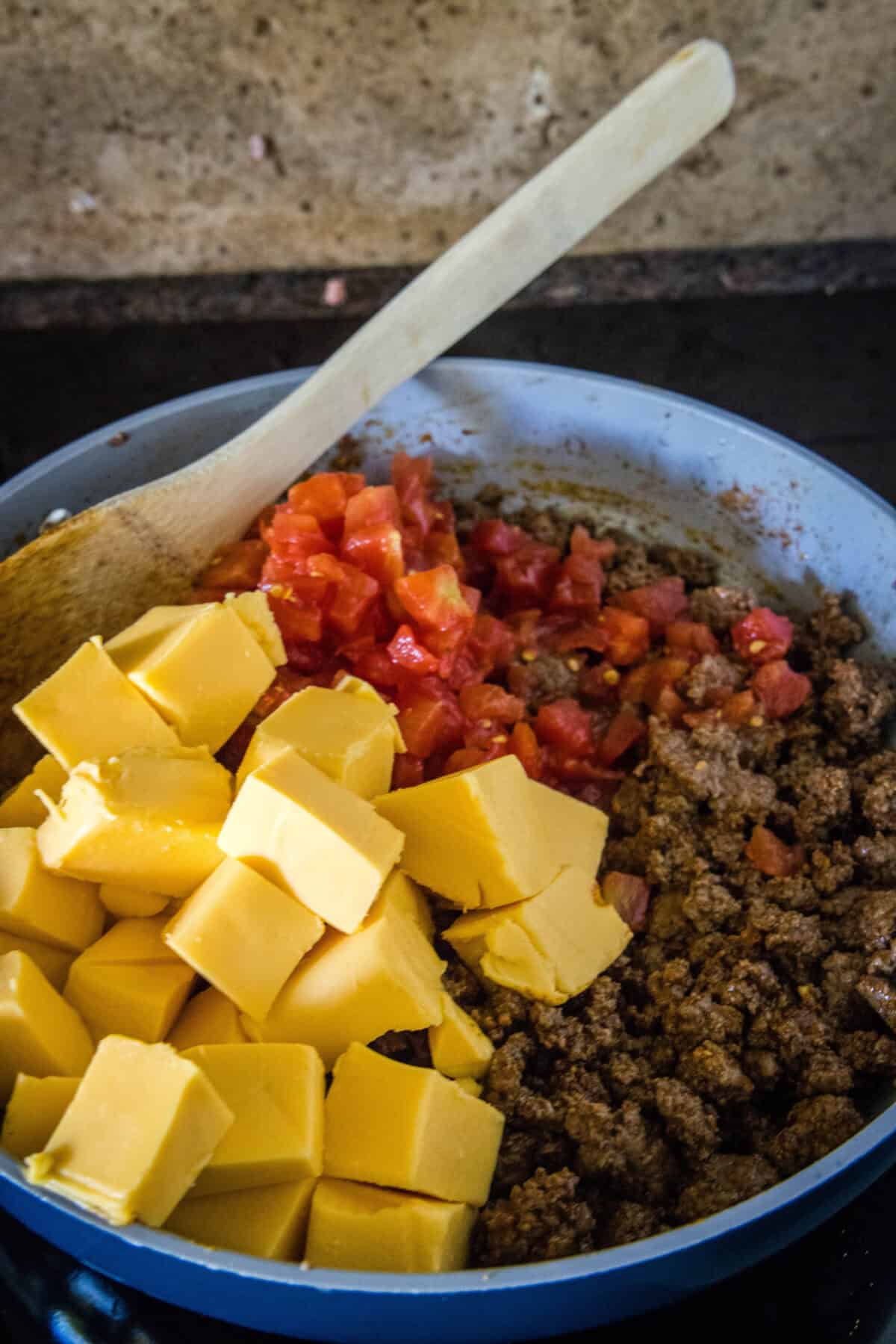 adding tomatoes and velveeta to taco meat in a skillet