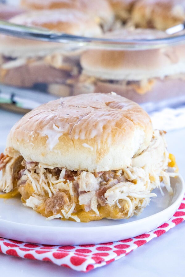 A chicken bacon ranch slider on a plate with more sliders in a glass baking dish in the background.