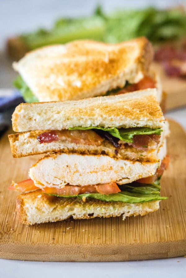 Close up of one half of a chicken club sandwich on a wooden cutting board.