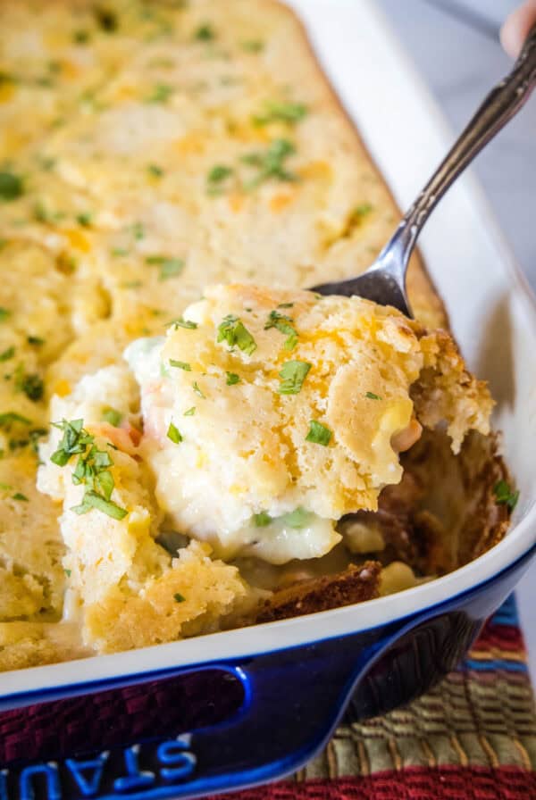 A spoon scooping a serving of chicken cobbler from the corner of a casserole dish.