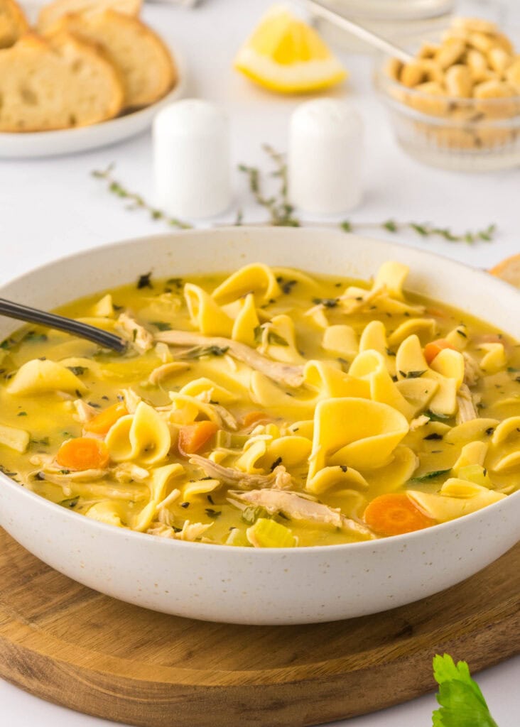 a bowl of chicken noodle soup on a board