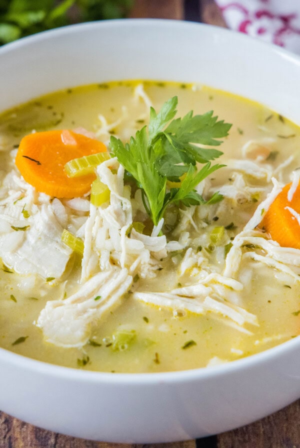 A bowl of chicken rice soup garnished with fresh parsley on a wooden table.