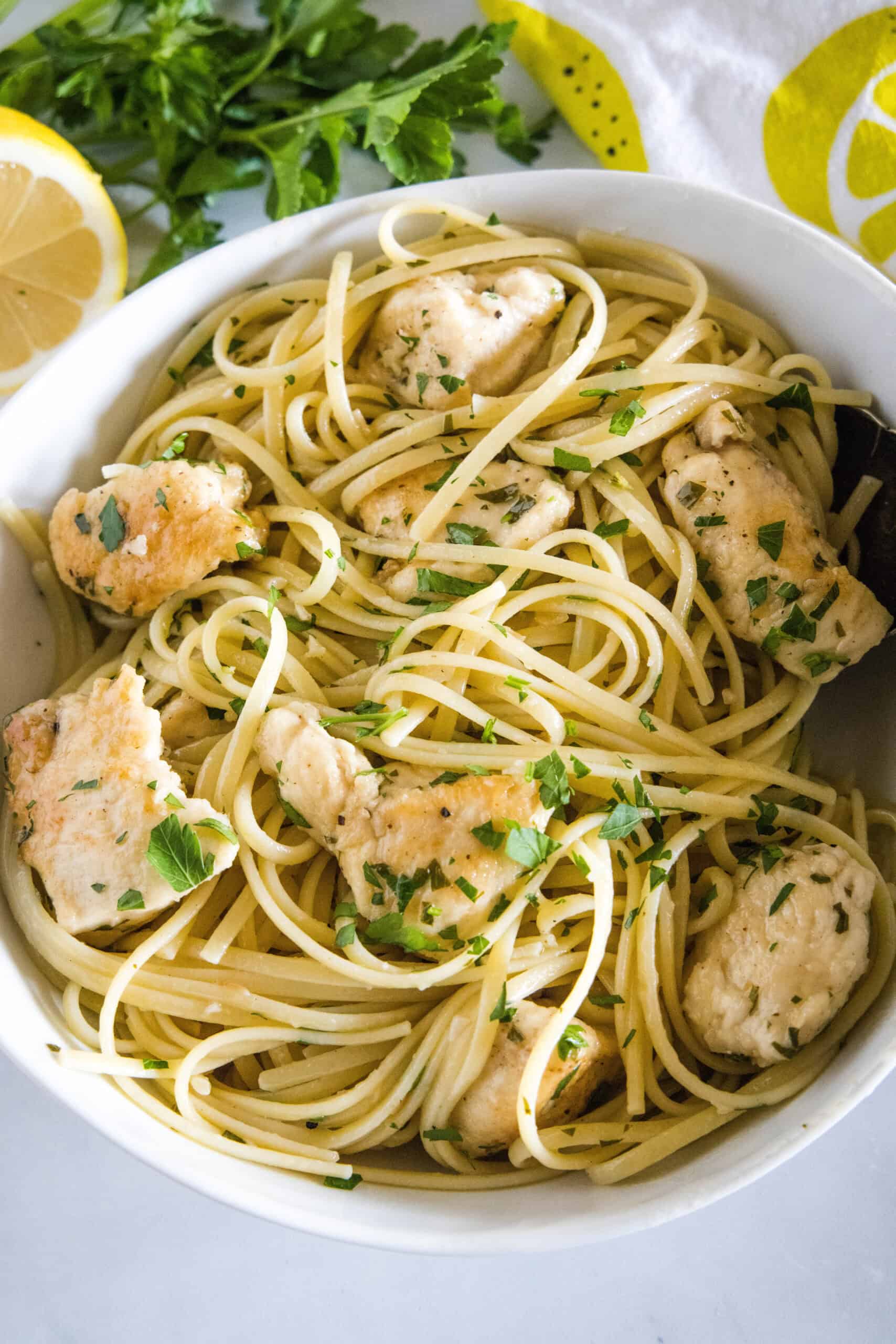 Overhead view of chicken scampi with spaghetti in a white bowl.