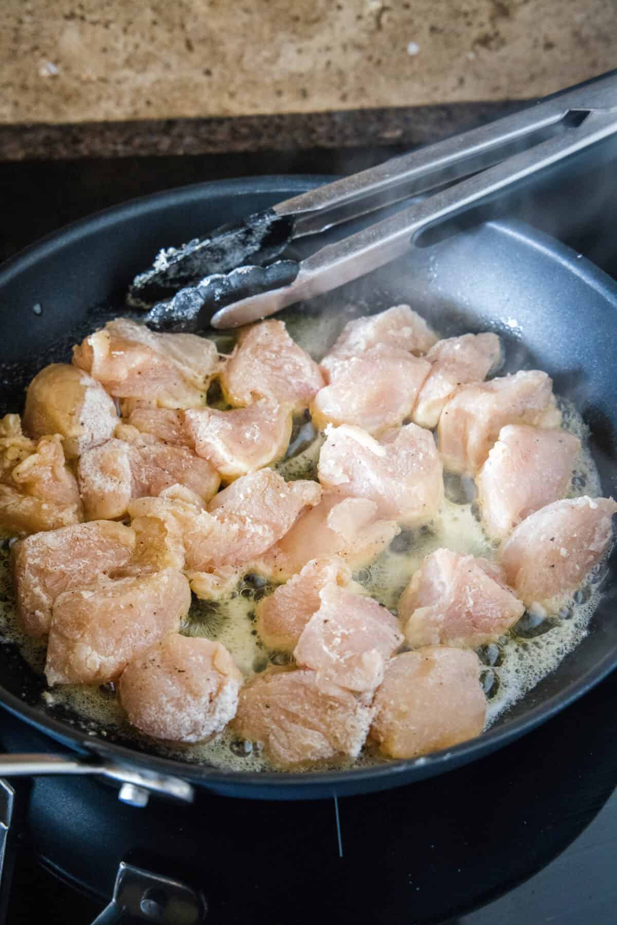 Chicken pieces sautéing in a skillet.