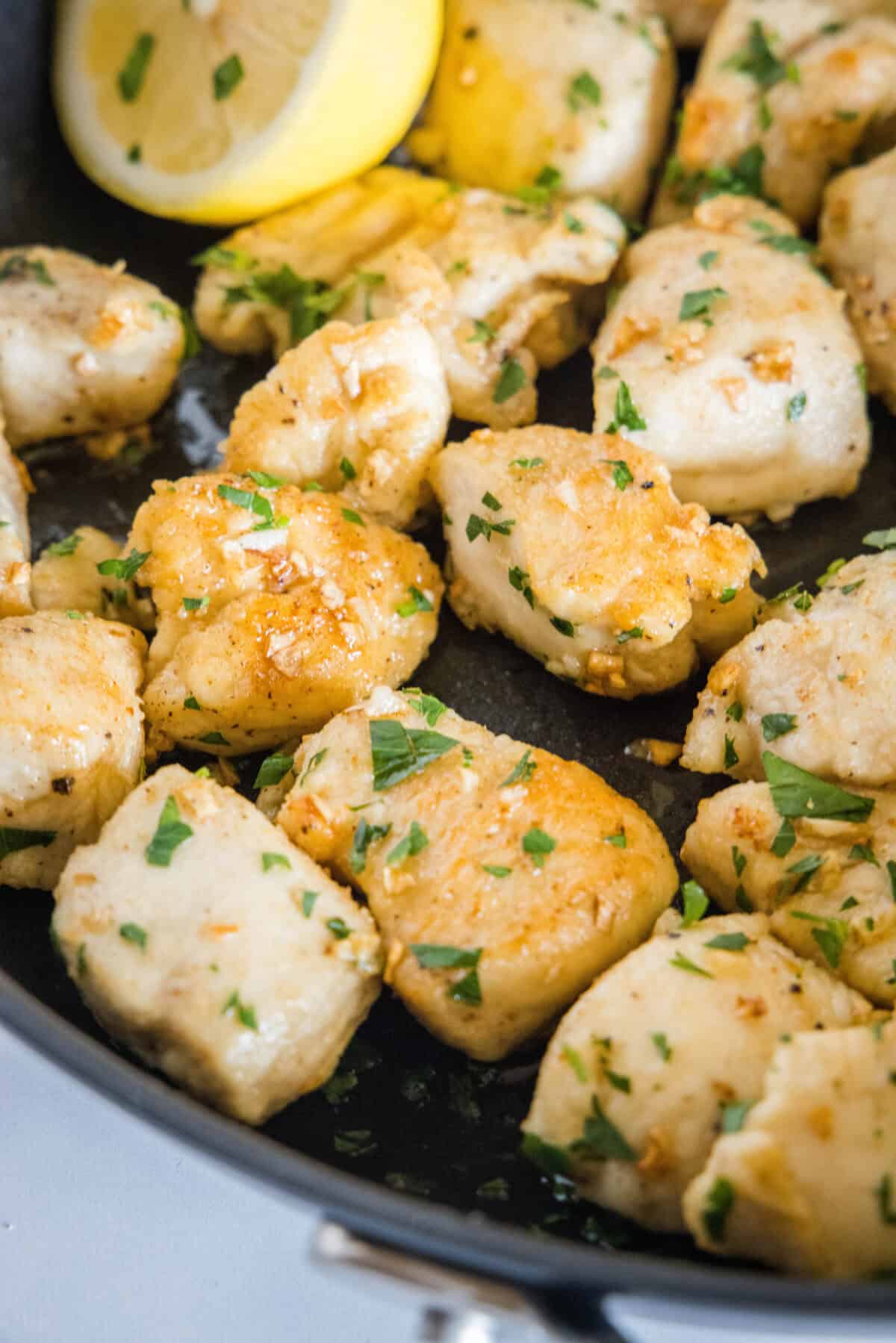 Close up of seared chicken pieces garnished with parsley in a skillet.