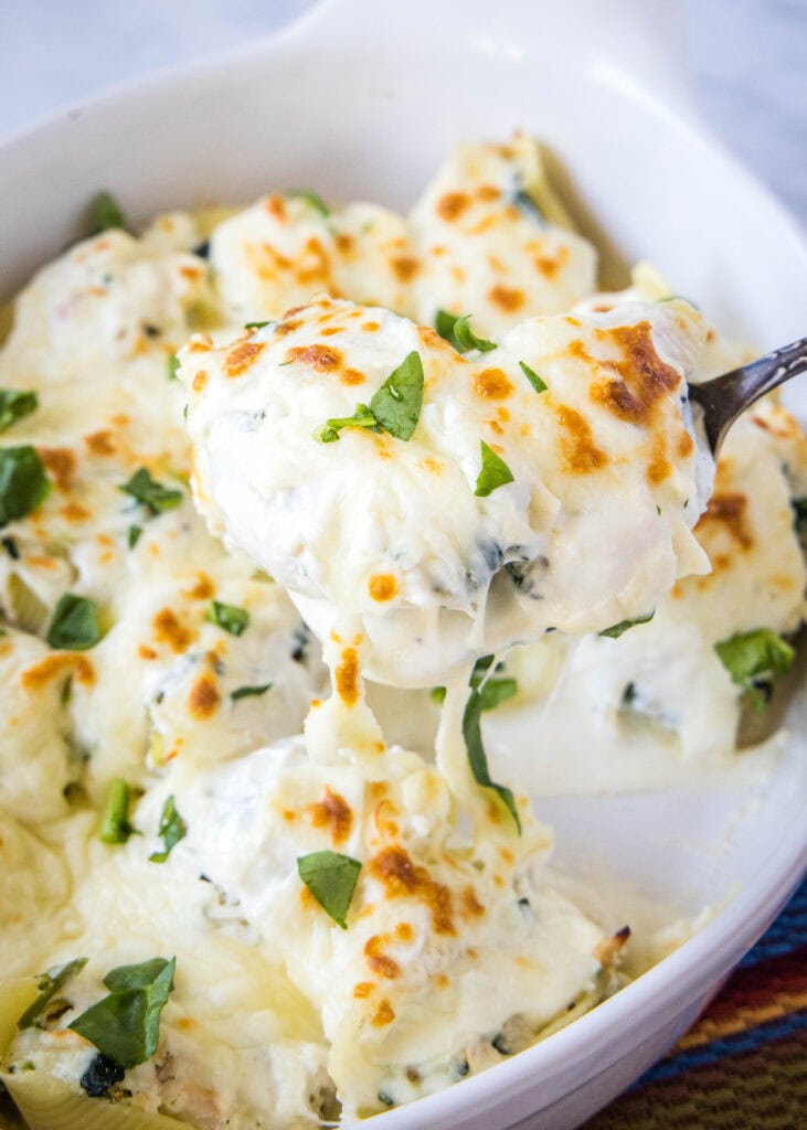 scooping chicken stuffed shells out of baking dish