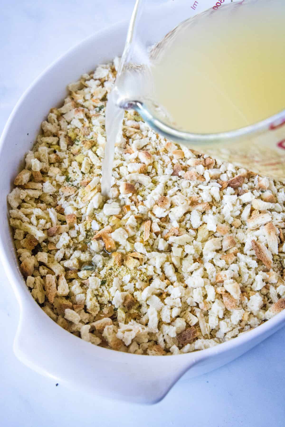 pouring chicken broth over stuffing mixture