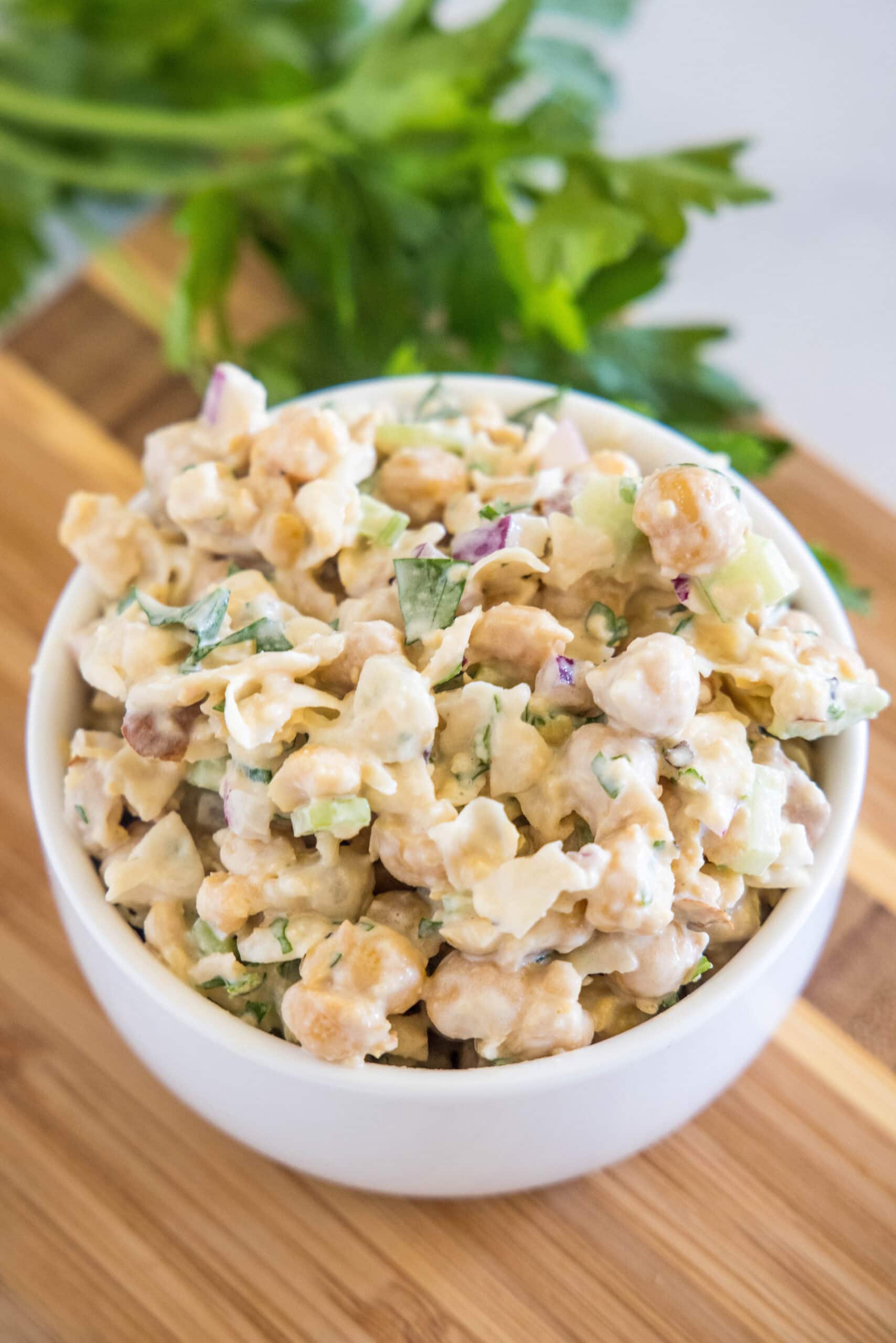 A bowl of chickpea chicken salad on a wooden cutting board.