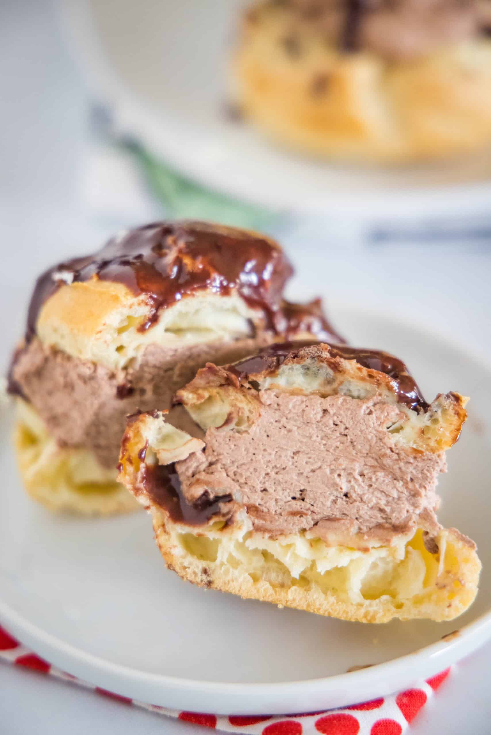 A chocolate cream puff topped with chocolate ganache cut in half on a white plate.