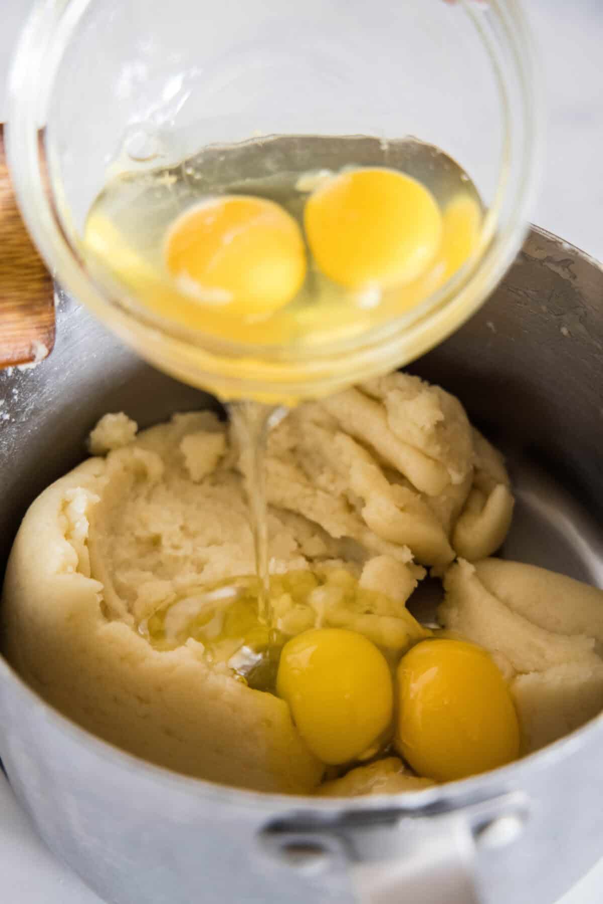 Eggs being added to puff pastry dough in a saucepan.