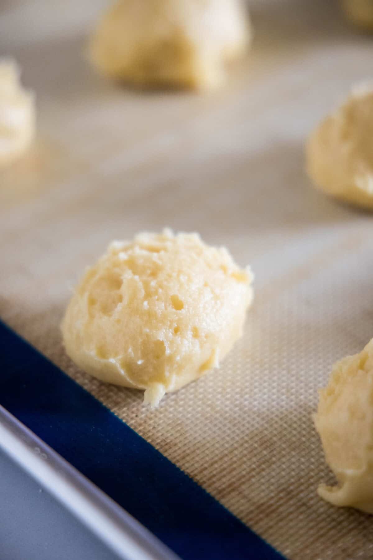 Scoops of pastry dough portioned onto a lined baking sheet.